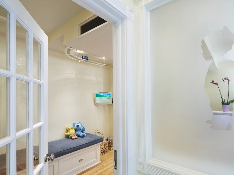 Pediatric dental office playroom with cushioned bench, toys, and flowers by window.