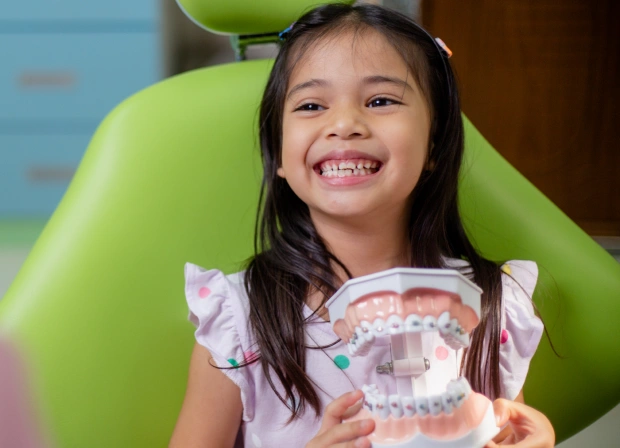 Young girl smiling in dental chair holding orthodontic model display.