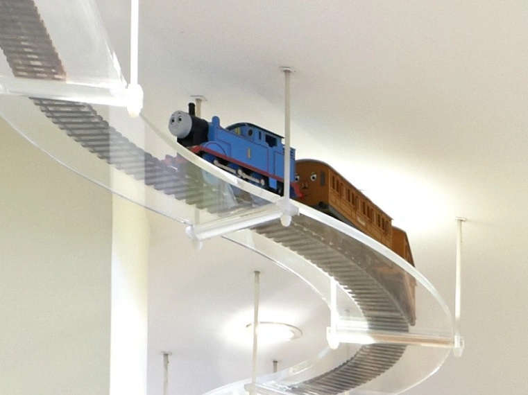 Toy train traveling on curved transparent track mounted on ceiling in dental office.