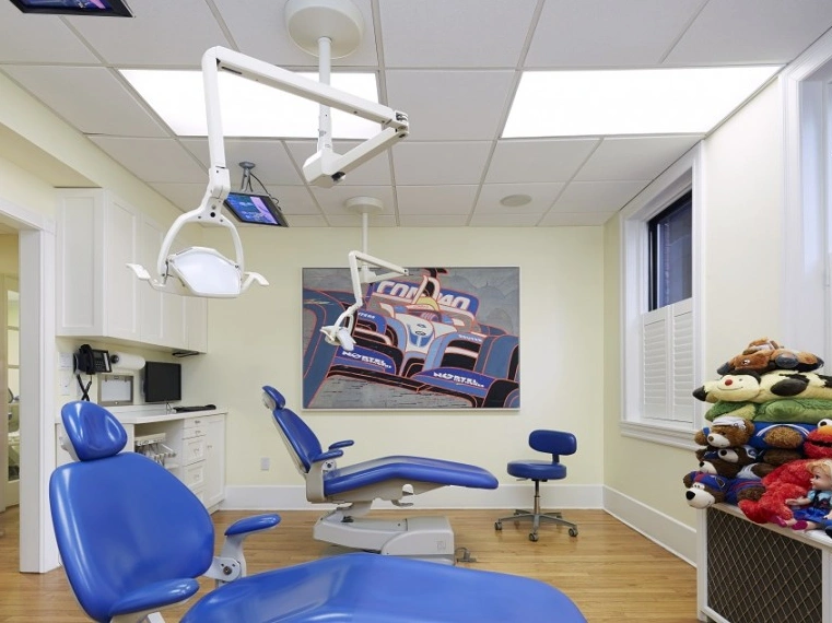 Pediatric dental operatory with blue equipment, racing car poster, and stuffed animals for child patients.