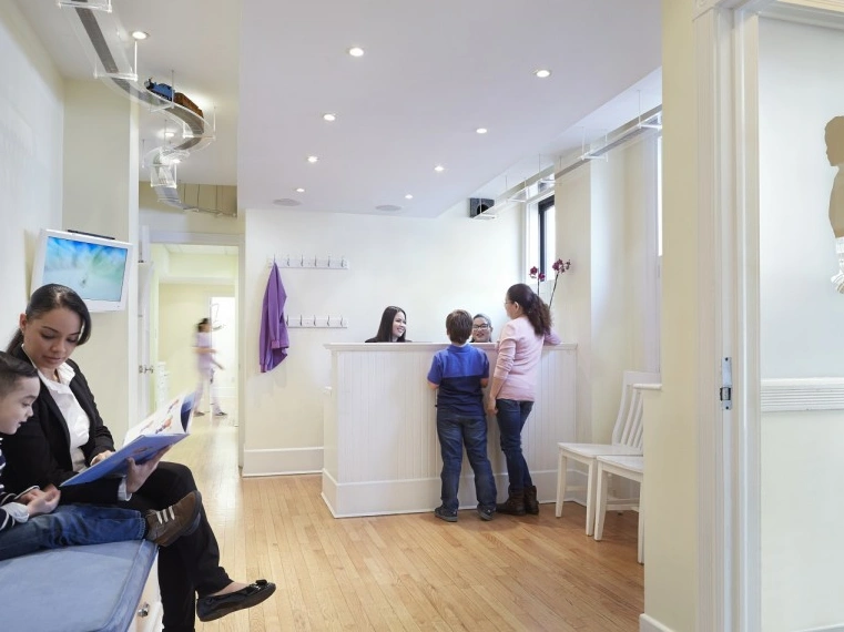 Pediatric dental office reception area with staff assisting young patients at the front desk.