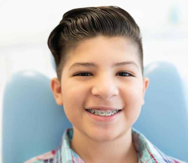 Young boy with braces smiling at camera in dental office setting with blue background.