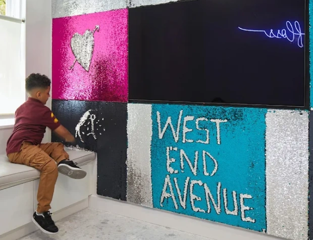 Young child touching interactive dental office mural featuring "West End Avenue" text and colorful panels.