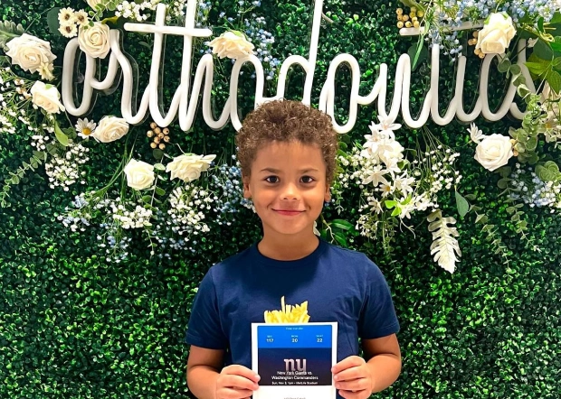Child holding dental award in front of floral graduation backdrop with "Graduation" sign.