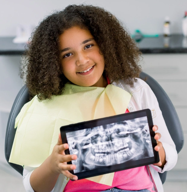 Young patient displays dental X-ray on tablet in pediatric dental office examination chair.