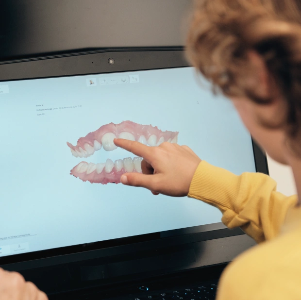 Child in yellow shirt pointing at dental model on computer screen showing teeth anatomy.