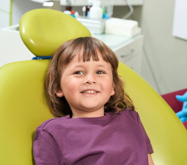 Young child smiling in yellow dental chair at pediatric dental office