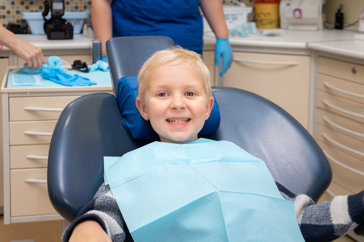Young boy smiling in dental chair wearing protective bib during pediatric checkup.