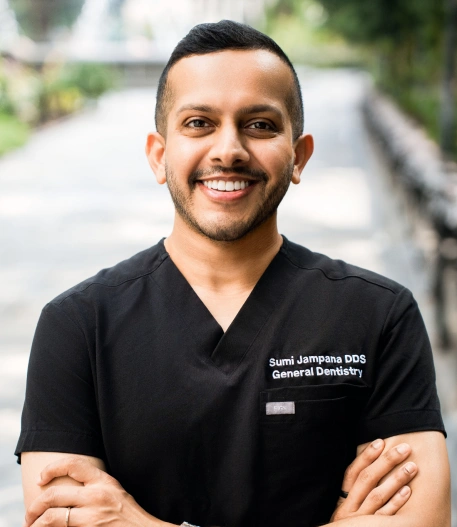 Headshot of dentist Dr. Sumi Jampana smiling outdoors in black scrubs embroidered with "Sumi Jampana DDS General Dentistry".
