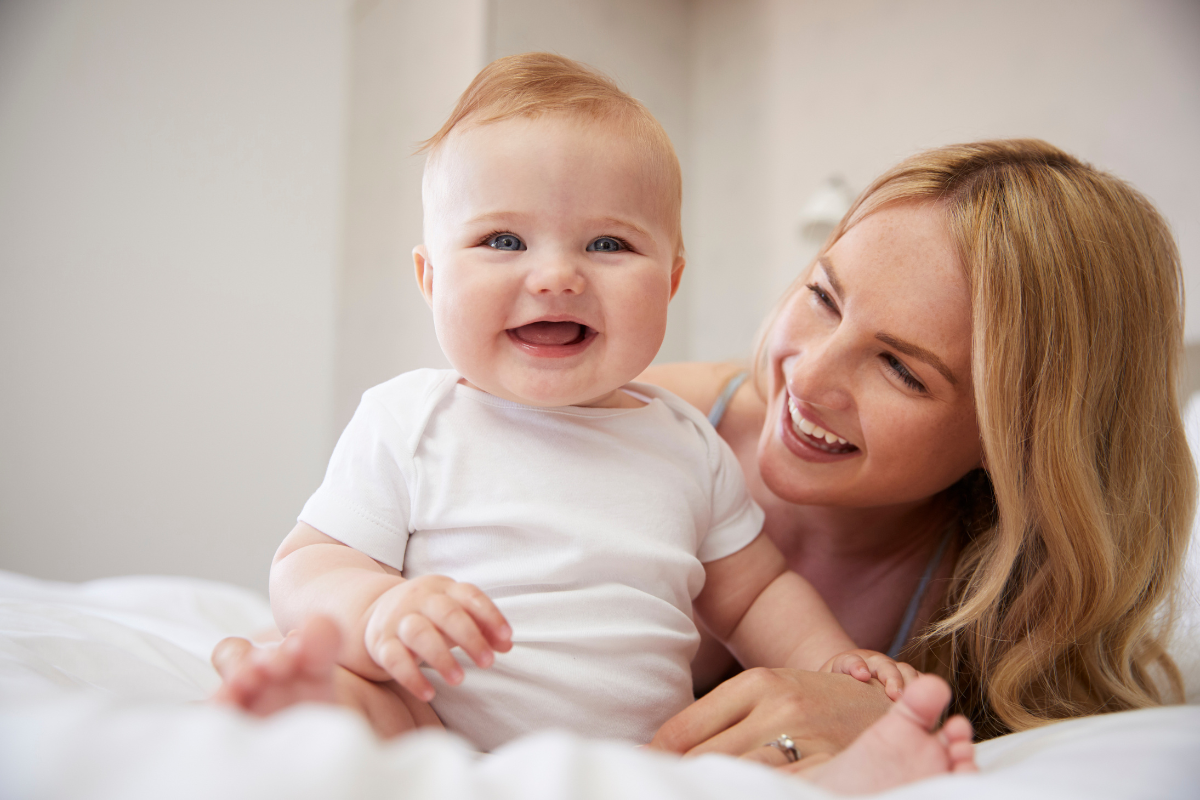Happy mother and smiling baby in white clothing, representing pediatric dental care and family wellness.